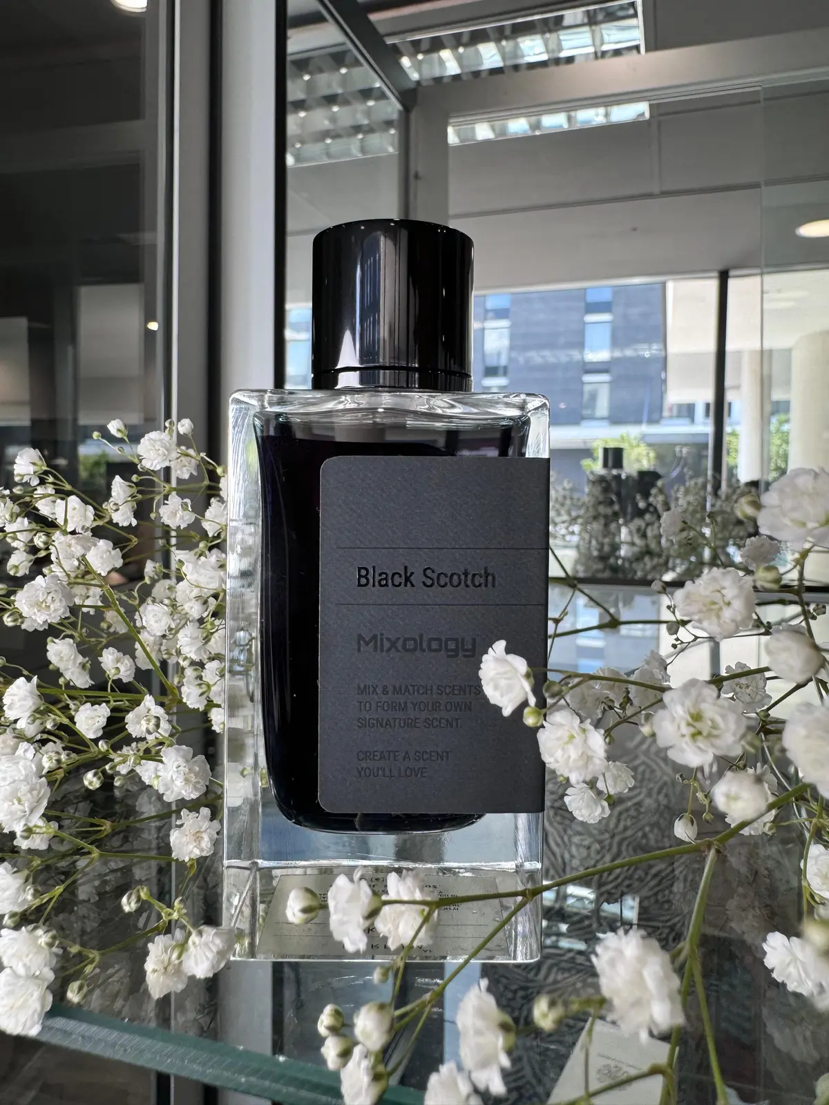 Mixology Black Scotch fragrance bottle displayed among white flowers