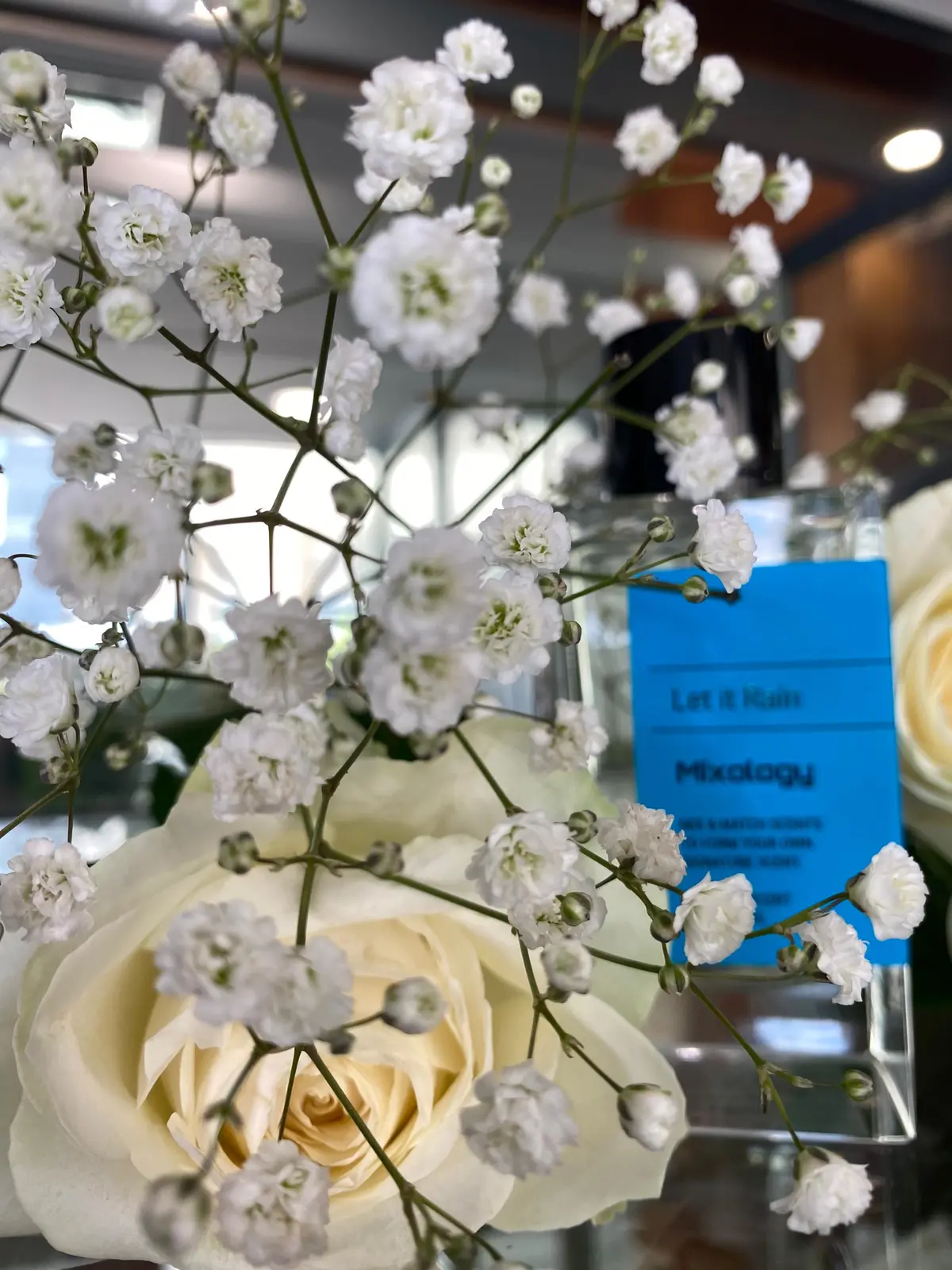 Mixology Let It Rain fragrance bottle displayed among white flowers